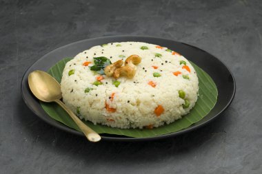 Samolina ya da rava upma 'dan yapılmış, en ünlü Güney Hindistan kahvaltı öğesi muz yaprağıyla güzelce hazırlanmış ve kızarmış fındık ve köri yapraklarıyla süslenmiş gri arka planda..