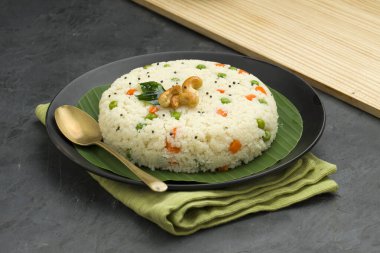 Samolina veya rava upma 'dan yapılmış upma, en ünlü Güney Hindistan kahvaltı öğesi siyah bir tabakta düzenlenir ve kaju fıstığı ve köri yapraklarıyla süslenir..