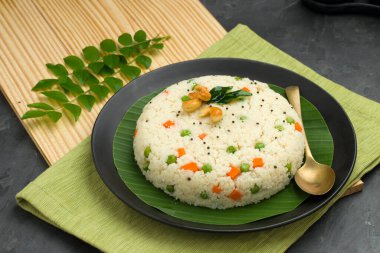 Samolina veya rava upma 'dan yapılmış upma, en ünlü Güney Hindistan kahvaltı öğesi, siyah bir tabakta düzenlenir ve kaju fıstığı ve köri yapraklarıyla süslenir..