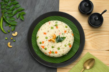 Samolina veya rava upma 'dan yapılmış upma, en ünlü Güney Hindistan kahvaltı öğesi siyah bir tabakta düzenlenir ve kaju fıstığı ve köri yapraklarıyla süslenir..