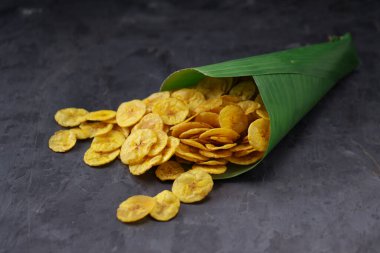 Kurutulmuş muz cipsi ya da muz waffle 'ı muz yaprağı konisinden gri desenli arka plana döküldü..