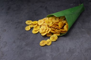 Kurutulmuş muz cipsi ya da muz waffle 'ı muz yaprağı konisinden gri desenli arka plana döküldü..