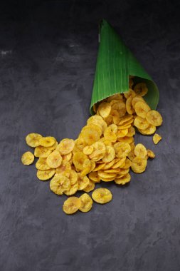 Kurutulmuş muz cipsi ya da muz waffle 'ı muz yaprağı konisinden gri desenli arka plana döküldü..