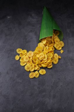 Kurutulmuş muz cipsi ya da muz waffle 'ı muz yaprağı konisinden gri desenli arka plana döküldü..