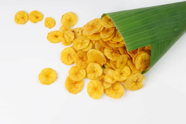 Dried banana chips or banana waffers spilled out from the banana leaf cone to the white textured background.