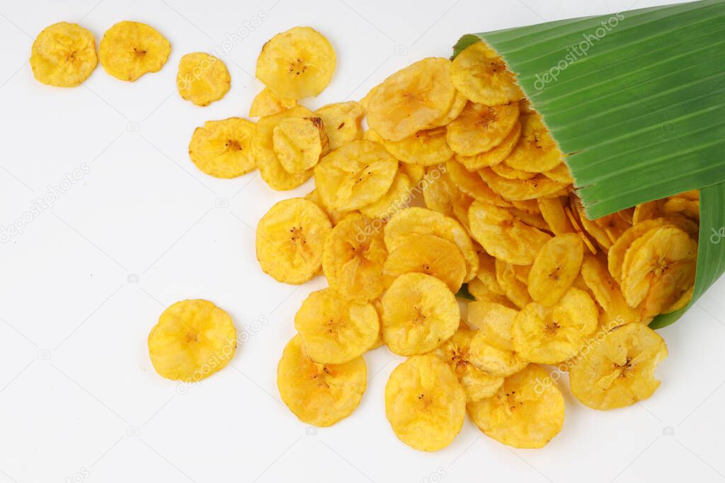Dried banana chips or banana waffers spilled out from the banana leaf cone to the white textured background.