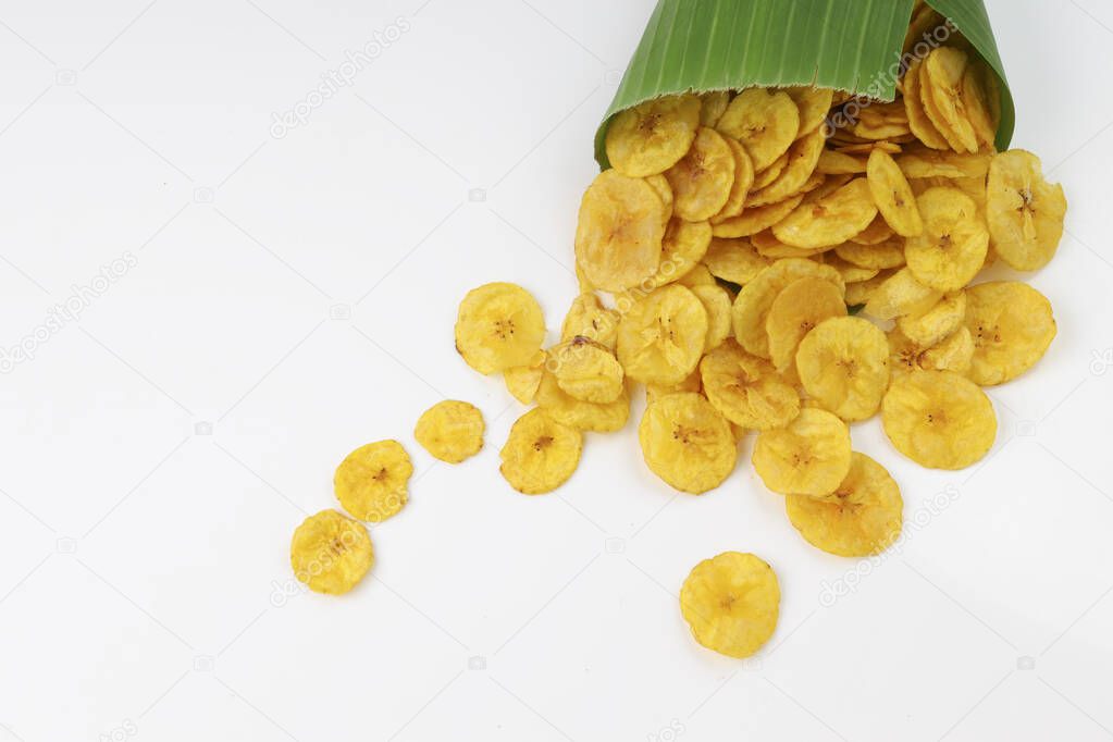 Dried banana chips or banana waffers spilled out from the banana leaf cone to the white textured background.