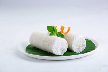 Puttu, buhar keki, beyaz çiğ pirinç puttu, Pacharisi maavu puttu _ kahvaltı öğesi pirinç unu kullanılarak yapılan havuç ve nane yaprağı ile süslenmiş ve beyaz arka planda muz yaprağıyla kaplanmış beyaz tabakta düzenlenmiş