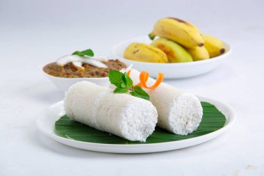 Puttu, buhar keki, beyaz çiğ pirinç puttu, Pacharisi maavu puttu ve kadala körili ve muzlu kahvaltı malzemesi havuç ve nane yaprağı ile süslenmiş ve beyaz arka planda muz yaprağıyla kaplı beyaz tabakta düzenlenmiş pirinç unu kullanılarak yapılır.