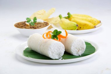 Puttu, buhar keki, beyaz çiğ pirinç puttu, Pacharisi maavu puttu ve kadala körili ve muzlu kahvaltı malzemesi havuç ve nane yaprağı ile süslenmiş ve beyaz arka planda muz yaprağıyla kaplı beyaz tabakta düzenlenmiş pirinç unu kullanılarak yapılır.