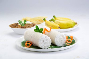 Puttu, buhar keki, beyaz çiğ pirinç puttu, Pacharisi maavu puttu ve kadala körili ve muzlu kahvaltı malzemesi havuç ve nane yaprağı ile süslenmiş ve beyaz arka planda muz yaprağıyla kaplı beyaz tabakta düzenlenmiş pirinç unu kullanılarak yapılır.