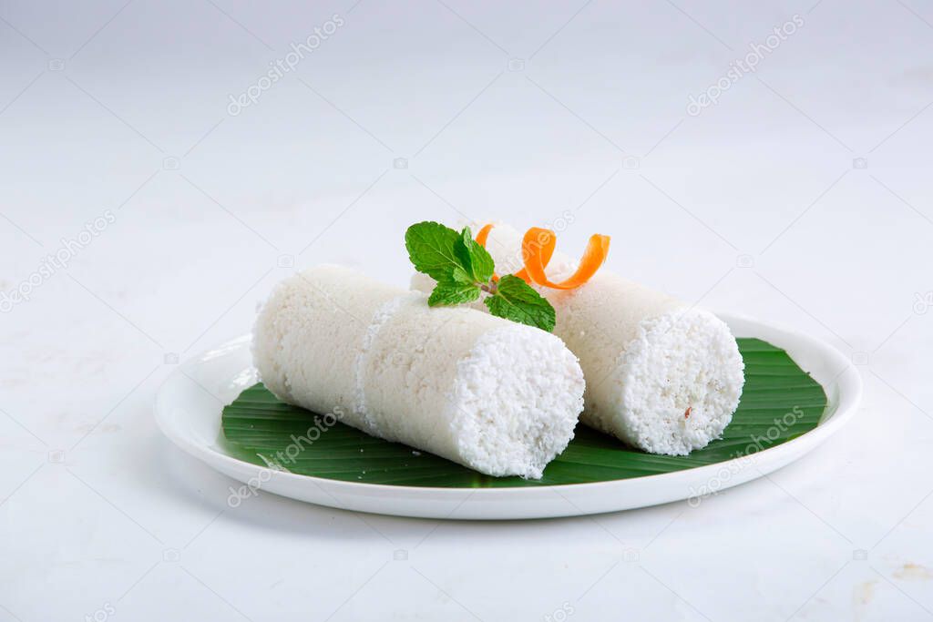 Puttu,steam cake ,white raw rice puttu , pacharisi maavu puttu _breakfast item made using rice flour which is garnished with carrot and mint leaf and arranged in white plate lined with banana leaf on white background