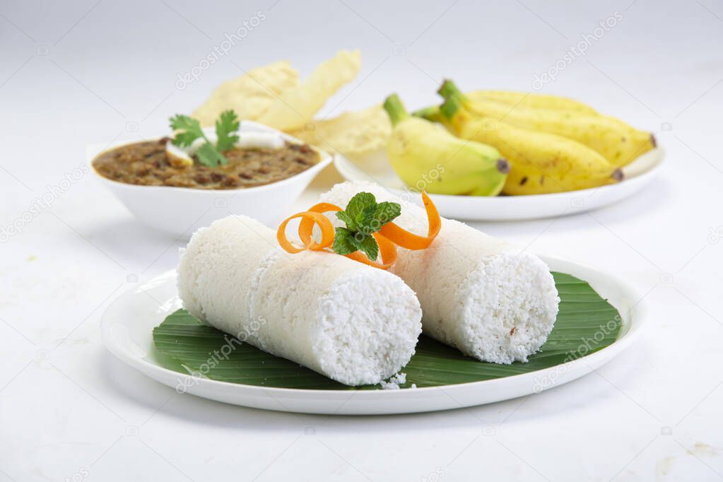 Puttu,steam cake ,white raw rice puttu , pacharisi maavu puttu with kadala curry and banana _breakfast item made using rice flour which is garnished with carrot and mint leaf and arranged in white plate lined with banana leaf on white background