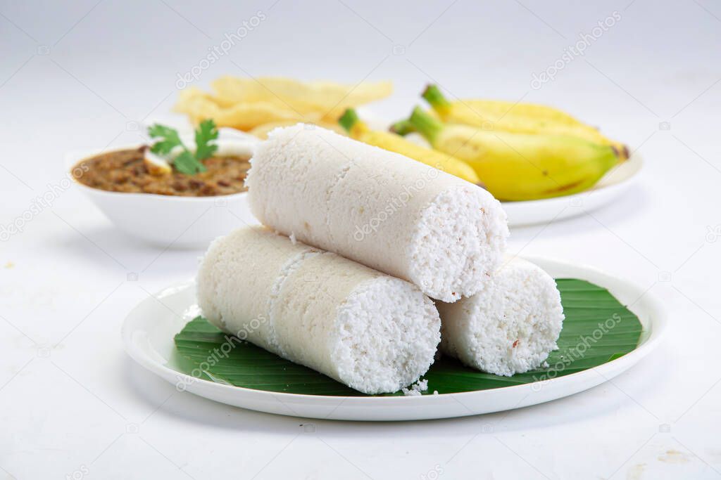 Puttu,steam cake ,white raw rice puttu , pacharisi maavu puttu with kadala curry and banana _breakfast item made using rice flour which is garnished with carrot and mint leaf and arranged in white plate lined with banana leaf on white background