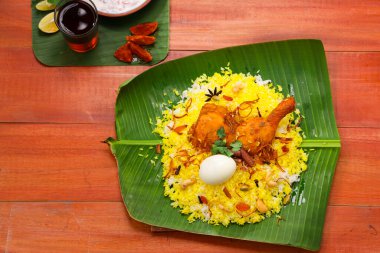 Kerala Tavuk dum biryani, geleneksel olarak muz yaprağı ve raita karışımı bir meze ve ahşap arkaplan veya dokuya sahip sıcak limon çayı, seçici bir odak noktası.