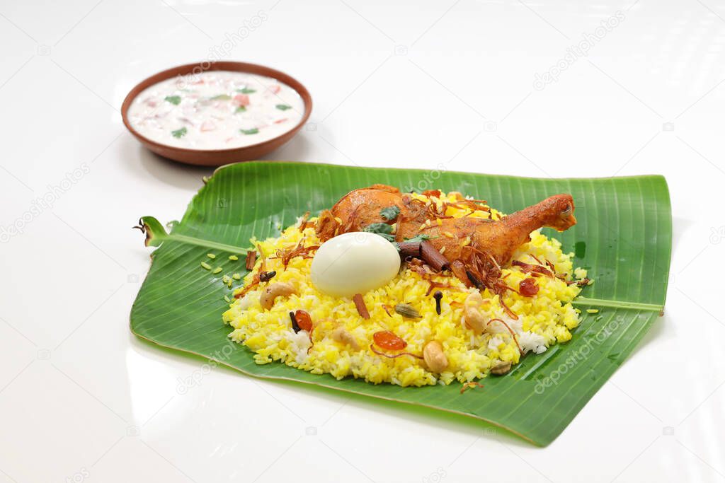 Kerala Chicken dum biryani ,arranged traditionally in a banana leaf  and raita as side dish with white  background or texture,selective focus