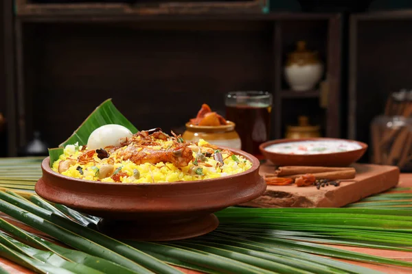 Chicken dum biryani , lemon pickle  and raita as side dish and hot lemon tea  with wooden  texture,kitchen background ,selective focus