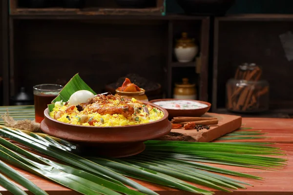 Chicken dum biryani , lemon pickle  and raita as side dish and hot lemon tea  with wooden  texture,kitchen background ,selective focus