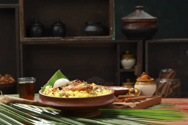Chicken dum biryani , lemon pickle  and raita as side dish and hot lemon tea  with wooden  texture,kitchen background ,selective focus