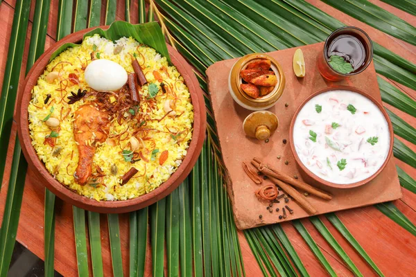 Chicken dum biryani , lemon pickle  and raita as side dish and hot lemon tea  with wooden  texture,kitchen background ,selective focus