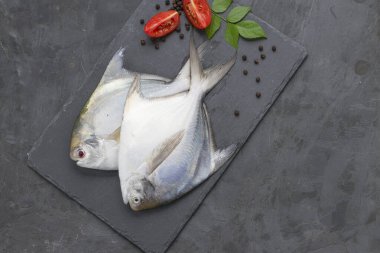 Çiğ beyaz Pomfrot, dikdörtgen şeklinde grafit bir yaprağa yerleştirilmiş, yanında domates dilimleri, karabiber ve köri yaprakları ve grafit renkli bir arkaplan..