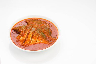 Beyaz pomfret masala körisi, Hint usulü, koyu kırmızı soslu ve yeşil biber, köri yaprakları ve beyaz arkaplanda beyaz bir seramik kasede düzenlenmiş malabar tamarind ile süslenmiş..