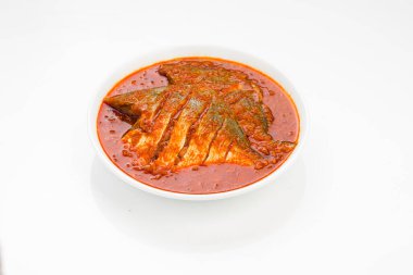 Beyaz pomfret masala körisi, Hint usulü, koyu kırmızı soslu ve yeşil biber, köri yaprakları ve beyaz arkaplanda beyaz bir seramik kasede düzenlenmiş malabar tamarind ile süslenmiş..