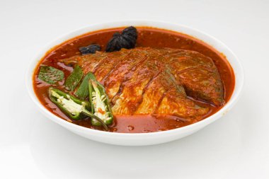 Beyaz pomfret masala körisi, Hint usulü, koyu kırmızı soslu ve yeşil biber, köri yaprakları ve beyaz arkaplanda beyaz bir seramik kasede düzenlenmiş malabar tamarind ile süslenmiş..