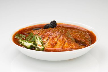 Beyaz pomfret masala körisi, Hint usulü, koyu kırmızı soslu ve yeşil biber, köri yaprakları ve beyaz arkaplanda beyaz bir seramik kasede düzenlenmiş malabar tamarind ile süslenmiş..