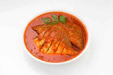 Beyaz pomfret masala körisi, Hint usulü, koyu kırmızı soslu ve yeşil biber, köri yaprakları ve beyaz arkaplanda beyaz bir seramik kasede düzenlenmiş malabar tamarind ile süslenmiş..
