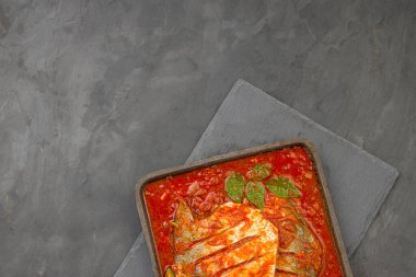  Beyaz pomfret masala körisi, Hint usulü, kalın kırmızı soslu ve yeşil biberli, köri yapraklı ve malabar tamarind ile süslenmiş gri arkaplanlı bir demir cızırtısında..