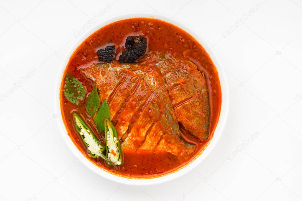 White pomfret masala curry , made in south indian style with thick red gravy and garnished with green chilli,curry leaves and malabar tamarind arranged in a white ceramic bowl with white colour background.