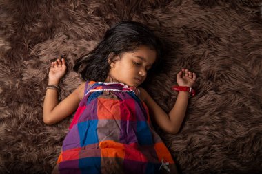 Uyuyan çocuk, farklı ifadeler gösteren bir kız çocuğu. Rengi çok yumuşak ve kahverengi olan bir sentetik halıda yatıyor.