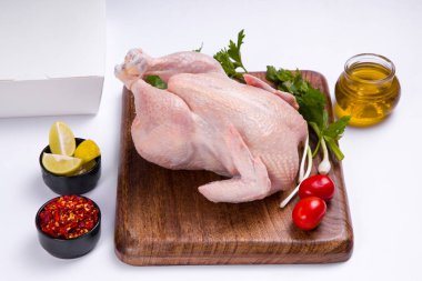 Ahşap tahtada derisi olan çiğ tavuk kısmen, küçük domates, taze soğan, kırmızı biber ve arka plan olarak beyaz renkli limon dilimleri, seçici odak, üst görünüm ile süslenmiş.