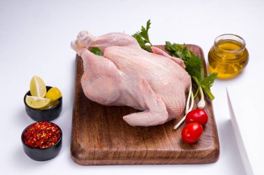 Ahşap tahtada derisi olan çiğ tavuk kısmen, küçük domates, taze soğan, kırmızı biber ve arka planda beyaz renkte limon dilimleri ile süslenmiş, seçici bir odak noktası.