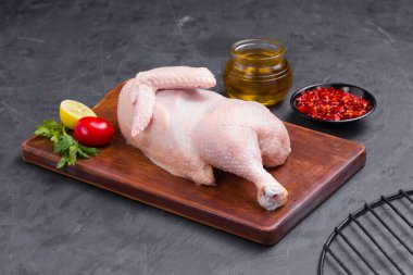 Çiğ yarım tavuk ve kahverengi ahşap tahta üzerinde sıralanmış ve kısmen, küçük domates, kırmızı biber, yağ ve limon dilimleri ile süslenmiş taş desenli ya da grafit renkli arkaplan, izole edilmiş