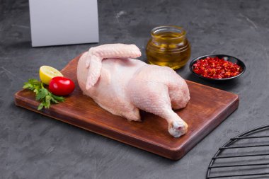 Çiğ yarım tavuk ve kahverengi ahşap tahta üzerinde sıralanmış ve kısmen, küçük domates, kırmızı biber, yağ ve limon dilimleri ile süslenmiş taş desenli ya da grafit renkli arkaplan, izole edilmiş