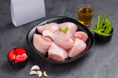 Çiğ tavuk biryani siyah kabın üzerinde derisiz kesilmiş ve kişniş yaprağı, sarımsak, domates dilimleri, taze yeşil biber ve grafit renkli arkaplanda teslimat kutusuyla süslenmiş.