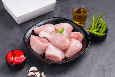 Çiğ tavuk biryani siyah kabın üzerinde derisiz kesilmiş ve kişniş yaprağı, sarımsak, domates dilimleri, taze yeşil biber ve grafit renkli arkaplanda teslimat kutusuyla süslenmiş.