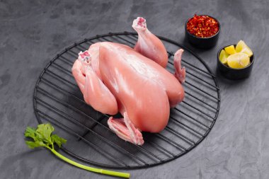 Taze çiğ tavuk, kısmen yaprak ve küçük kaseler dolusu gevrek ve limon dilimleri ile birlikte gri dokulu arka planda ızgaraya konur.