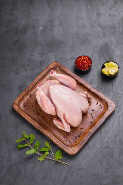 Tahtaya serpilmiş taze çiğ tavuk ve nane yaprağı ile süslenmiş küçük kaseler ve gri dokulu limon dilimleri.