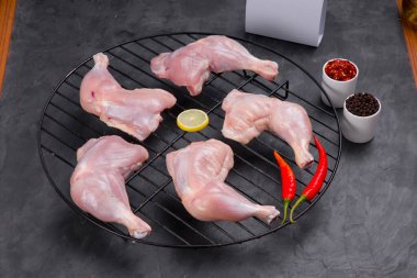 Izgarada derisi olmayan çiğ tavuk bacağı ve limon dilimleri ile süslenmiş kırmızı biber taneleri ve gri ya da grafit desenli arka planda biber.