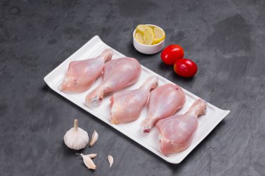 Domates, limon dilimleri ve gri arka planda sarımsaklı tavuk budu.