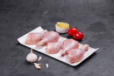 Domates, limon dilimleri ve gri arka planda sarımsaklı tavuk budu.