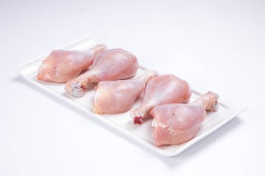 Beyaz masa donanımına yerleştirilmiş çiğ tavuk butları beyaz arka planda