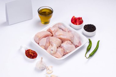 Çiğ köri soslu tavuk derisi beyaz tabağa dizilmiş ve sarımsak, siyah biber, yeşil biber, domates dilimleri, beyaz arka planda yağ ve kırmızı biber ile süslenmiş.