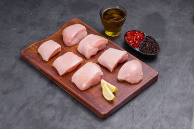 Çiğ tavuk kızartması ahşap tahtada derisiz kesilmiş ve yağla süslenmiş, limon dilimleri, soğuk tanecikler ve taş desenli karabiber ya da grafit renkli arka plan