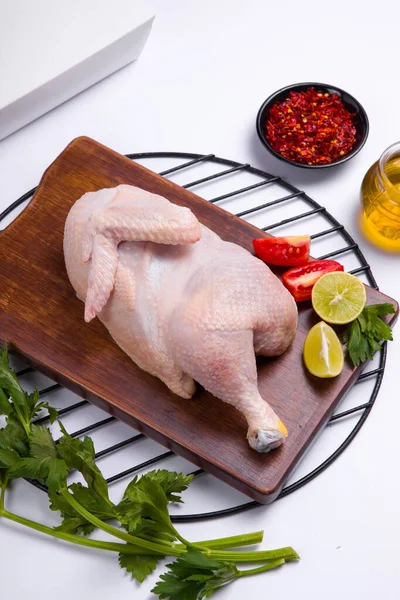 Raw half chicken with skin arranged on wooden board and garnished with parsely,small tomato ,oil and lemon slices on white colour background, selective focus