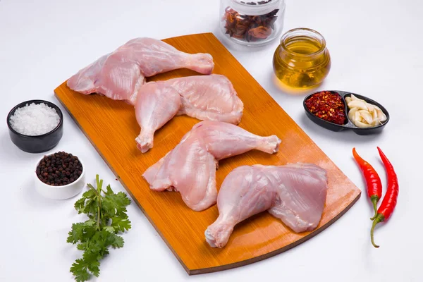 Raw whole chicken leg without skin arranged in wooden board and garnished with cooking ingrediants   on white textured  background