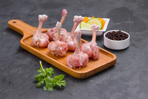 Raw chicken lollipop,six  pieces of chicken lollipop arranged on a serving board with black pepper,coriander leaf and cucumber slices on background with grey textured base